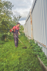 female worker mows the grass with a trimmer in the garden