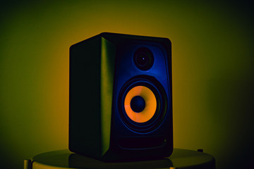 Active studio loudspeaker illuminated with blue light, isolated on a yellow illuminated background....