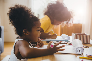 American Black preschool daughter kids doing homework learning education with her sister living...