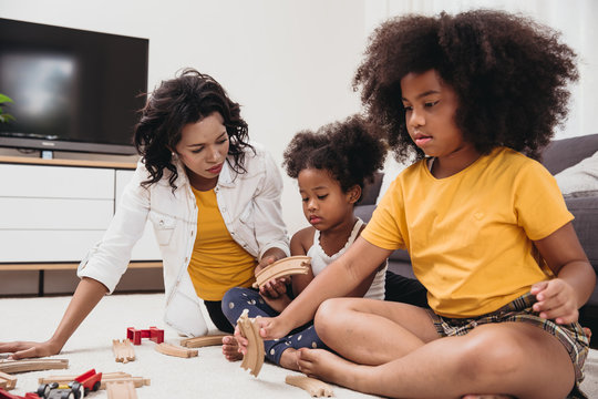 Single mom with two daughter playing toy in apartment. Nanny looking or childcare at home black people.