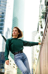 Vertical view. Portrait of a girl with short hairstyle, looking away posing on urban street, at buildings background