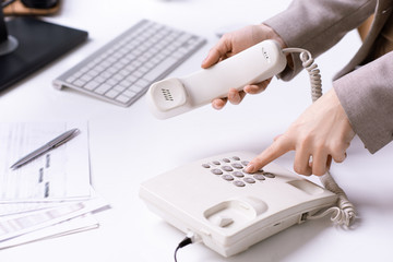 Hands of young office secretary dialing phone number and holding receiver