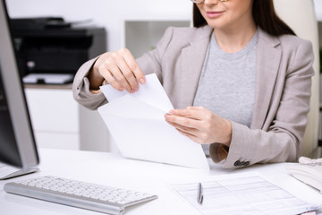 Hands of young businesswoman or banker putting folded paper into white envelope