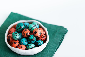 Painted red and blue quail eggs for Easter in small ceramic plate on green napkin on gray concrete background. Empty place for text and sign.