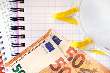 Protective Mask and 50 Euro banknotes on a white paper copybook background.