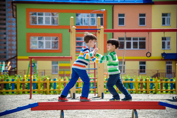 Two little school and preschool kids boys playing on playground outdoors together. children having competition standing on log with outdoor activities in summer sunny day
