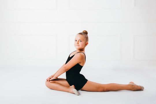Flexible little girl gymnast sitting in acrobatic pose on white background.
