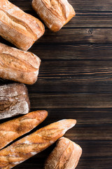 Various kind of bread - gold rustic crusty loaves of bread with wheat on wooden background. Still life captured from above (top view, flat lay).