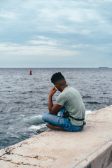 Latin guy in jeans sits on the promenade of the Caribbean