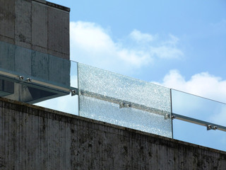 Shattered glass balustrade railing. broken laminated tempered safety glass. stone panel facade. construction and building industry concept. stainless steel glass bracket spiders. blue sky white clouds