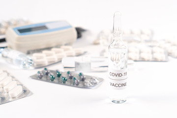 Coronavirus vaccine. Ampoule with COVID-19 medicine on a white table with medical equipment and capsules in packs. Close-up. Development and use of a cure for a new virus
