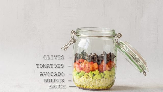Vegetarian salad in jar. Stop motion video. Empty jar is filing with vegetables, bulgur and feta cheese. Hand is taking jar away. Healthy eating, take away, lunch, dinner or homemade recipe.
