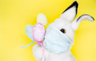 Close up Easter Bunny face in a medical mask with a bouquet of colorful eggs. The concept of Easter and quarantine during coronavirus. Like a postcard wishing you well