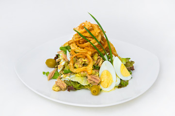 Seafood salad. Breaded fried squid rings, cod fish slices, green olives, eggs, lettuce. Decoration of bow feathers.