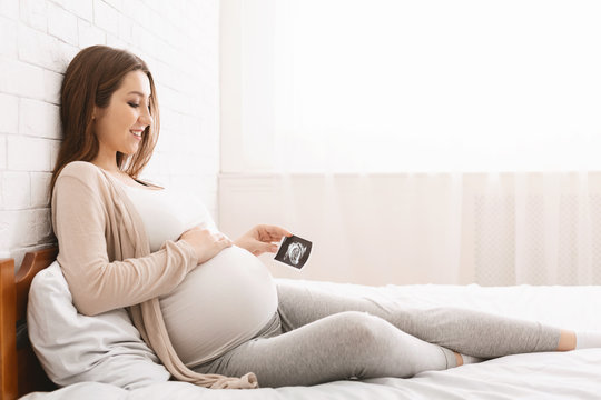 Pregnant woman enjoying future motherhood with first ultrasound photo