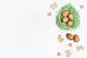 Wooden Easter eggs in a green paper straw nest, surrounded by wooden Easter bunnies and heart decorations, on a white background.