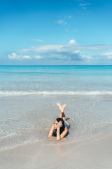 Fototapeta na wymiar Girl lies in blue water on the sandy beach