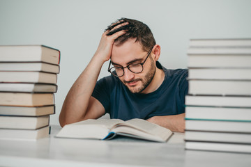 Young white European brunette man nerd in glasses teaches lessons, reads books, studied at university, prepares for exams, has many books at home in white backround table.