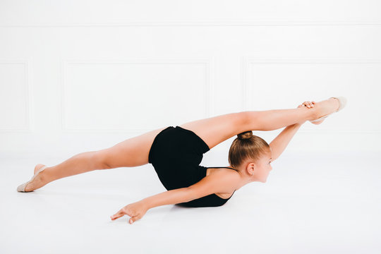 Flexible little girl gymnast doing splits in acrobatic pose on the floor on white background.