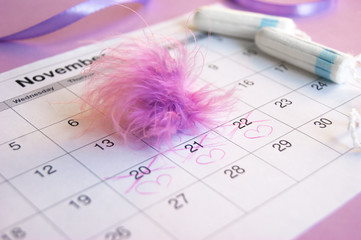 Menstrual pads and tampons on menstruation period calendar with on lilac background.