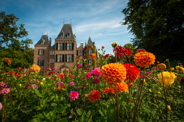 Garden with flowering dahlias in shades of orange and red in front of Keukenhof castle on a sunny day 