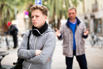 Frowning teenager listening to reprimanding from father