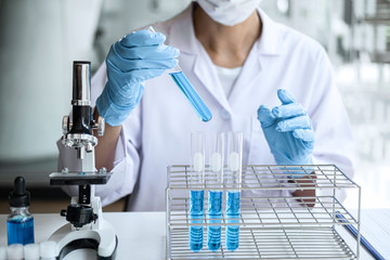 Biochemistry laboratory research, Scientist or medical in lab coat holding test tube with Using Microscope reagent with drop of color liquid over glass equipment working at the laboratory