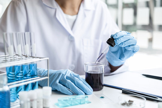 Scientist or medical in lab coat holding dropper with reagent, mixing reagents in glass flask, glassware containing chemical liquid, laboratory research and testing of Microscope