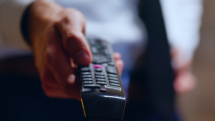 Close up of businessman relaxing after work using tv remote control