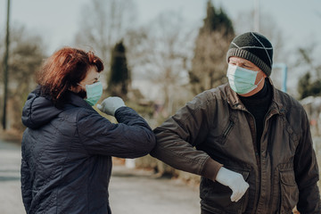 two seniors wearing facial masks and gloves greeting with hand sign