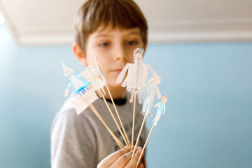School kid boy making paper doll theatre. Happy child creating figures and performing stage play during quarantine time at home. Active creative boy staying at home.