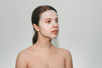 Obraz premium Portrait of young beautiful european woman with blue eyes with collagen silicone fabric with white mask on face on white background. Beauty treatments, the secret of youth, beauty, health.