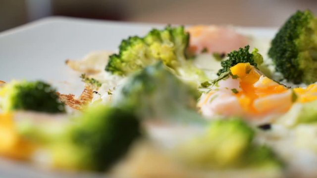 A womans hand lifts a broccoli fried egg with a fork. Close up