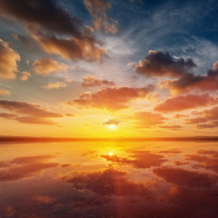 Beautiful sunset landscape with a lake, dramatic golden sky above reflects in the water.
