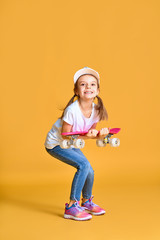 Stylish funny girl wearing white t-shirt, blue jeans and sneakers, holding skateboard over yellow background.
