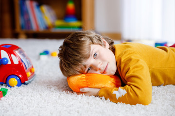 Close-up portrait of little blond kid boy playing at home with toys. Happy smiling child in casual clothes