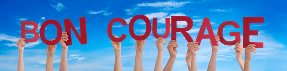 People Hands Holding Colorful French Word Bon Courage Means You Can Do It. Blue Sky As Background