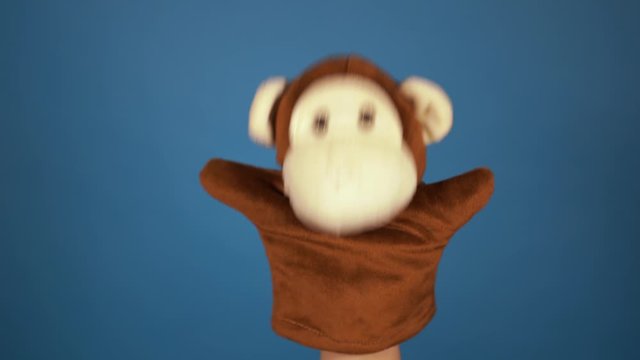 Soft puppet toy on hand on blue background. Concept of puppet show. Close-up of hand with puppet monkey.