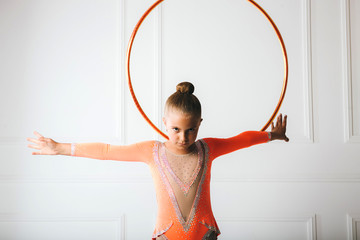 Beautiful serious fit gymnast girl in sportswear peach dress posing with athletic hoop on her...