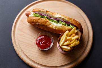 Hot Dogs with French fries and ketchup on wooden plate.