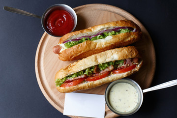 Two hot dogs and sause lying on the wooden plate. Mock up.
