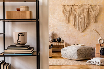 Interior design of oriental living room with beige macrame, big pouf, design furniture, shelf, carpet and elegant personal accessories in modern home decor.
