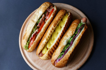 Three hot dogs lying on the wooden plate.