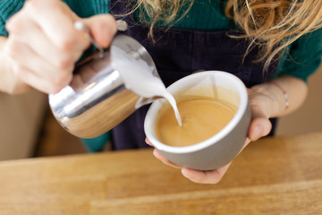 Girl barista is serving coffe with latte art inside the bright cafeteria 