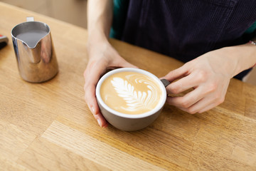 Girl barista is serving coffe with latte art inside the bright cafeteria 