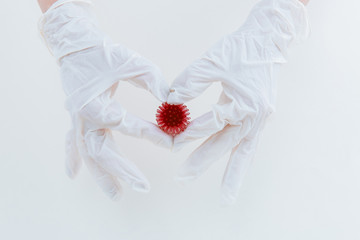 Hands in white medical gloves near an abstract viral model of coronavirus.