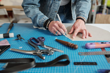 Hands of young craftsman bending over table while outlining paper pattern