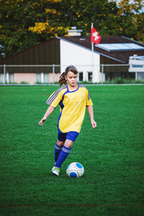 Young girl playing football at stadium with local girls football team. Small city stadium located in Switzerland. Swiss flag at background.