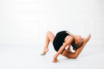 Fototapeta na wymiar Young girl in a black dress doing gymnastics pose, forehead touches the heel, on white background