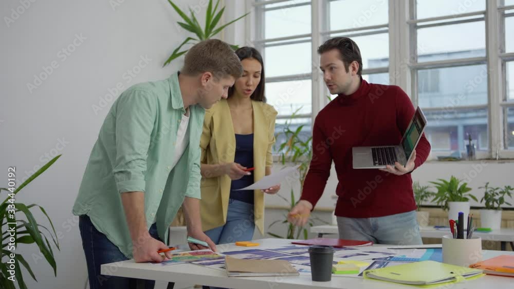 Wall mural young startup team of three standing around table in office and discussing application design templa